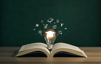 Lightbulb on a book with graduation hat, and education icons.