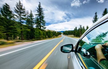 A close up a the side of car driving down the road and another care ahead in the background