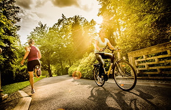 Two people on a park trail, one person is running one direction and the other person is riding a bike in the other direction.