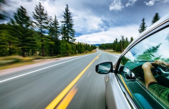 A car driving down a road with trees in the background.