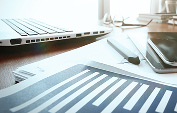 Close-up of a desk with a laptop, smart phone, tablet and documents.